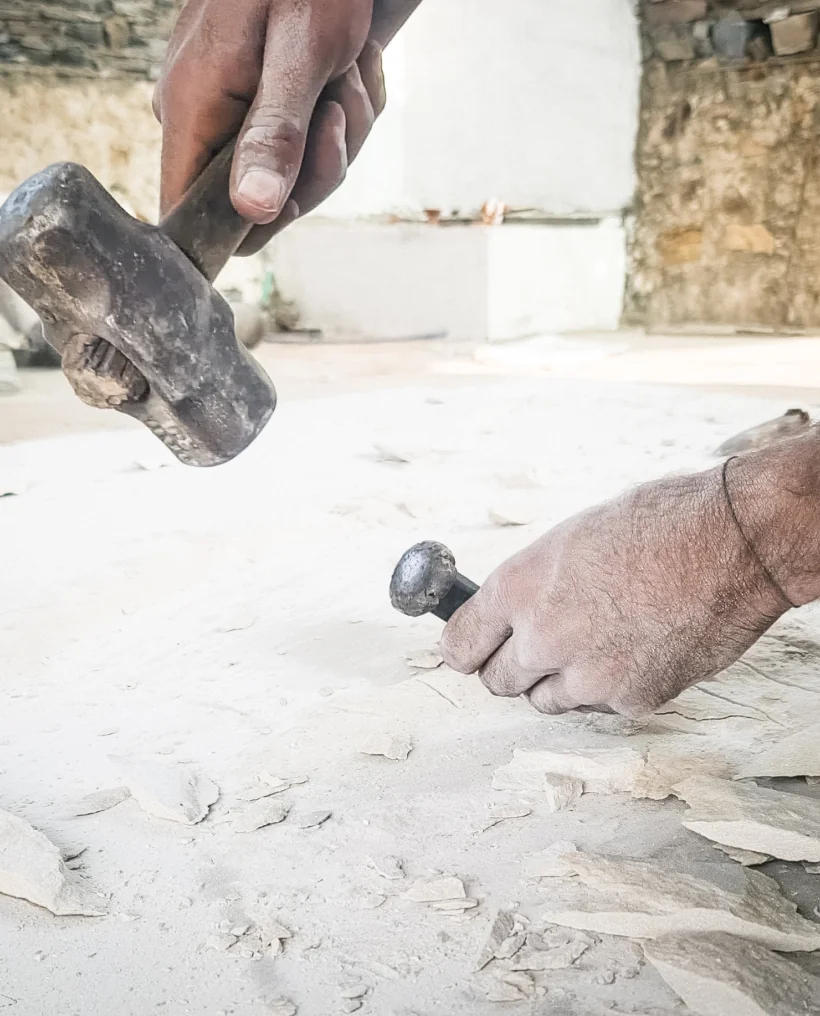 Handwerker bearbeitet einen hellen Stein mit Hammer und Meißel, um maßgeschneiderte Steinoberflächen für stonearts® Akustikpaneele und individuelle Wandverkleidungen zu schaffen.